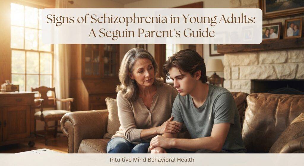 A photorealistic photograph capturing a quiet, intimate moment of mutual support in a sunlit, comfortable living room of a historic Central Texas home near Seguin. An older woman, a concerned parent, sits beside a young adult child on a plush leather sofa. The parent has a gentle, worried expression and is holding the child's arm; the child is looking down with a pensive, averted gaze, conveying a shared emotional burden. A large window on the left lets in warm, golden afternoon light, illuminating antique wooden furniture and framed family photos on a limestone mantelpiece. In the upper third of the image, a modern, clean, semi-transparent text overlay reads: "Signs of Schizophrenia in Young Adults: A Seguin Parent's Guide". At the bottom of the image, a subtle footer displays the text: "Intuitive Mind Behavioral Health".