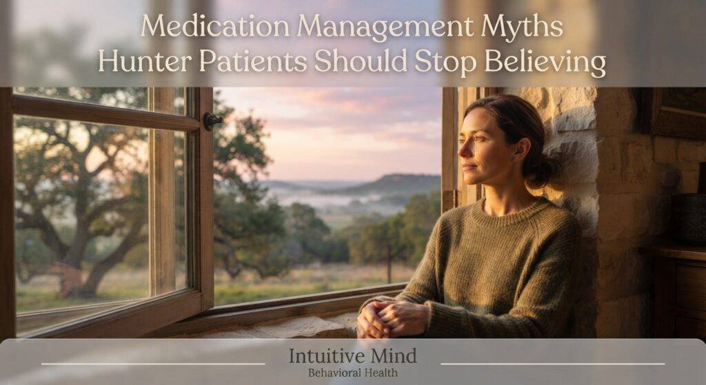 A photorealistic photograph capturing an adult woman in a quiet, thoughtful moment. She is sitting by a large, rustic wooden window, looking out at a sweeping view of the rolling Texas Hill Country during a warm, golden sunrise. The atmosphere conveys a sense of deep relief and renewal. A semi-transparent overlay in the upper third contains the modern text: "Medication Management Myths Hunter Patients Should Stop Believing". A subtle footer at the bottom of the image displays the text: "Intuitive Mind Behavioral Health".