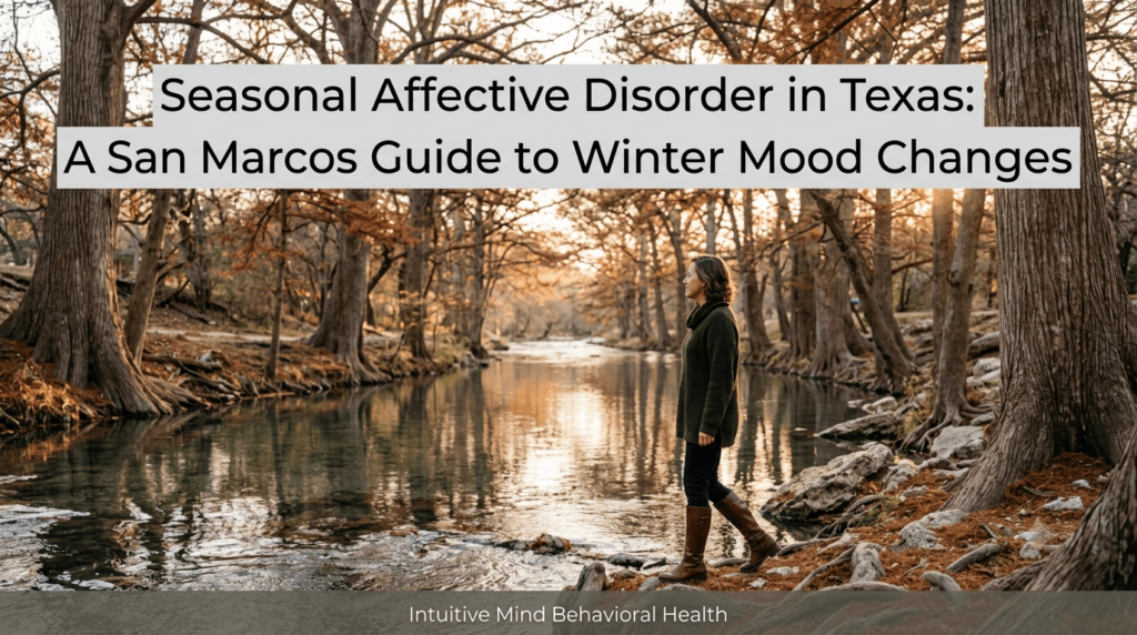 A photorealistic late afternoon scene along the calm, reflective San Marcos River lined with large, bare cypress trees and autumnal foliage. A woman wearing a green sweater and brown boots walks along the rocky riverbank under soft winter sunlight. A semi-transparent overlay at the top displays the title 'Seasonal Affective Disorder in Texas: A San Marcos Guide to Winter Mood Changes', with a subtle gray banner at the bottom reading 'Intuitive Mind Behavioral Health'.