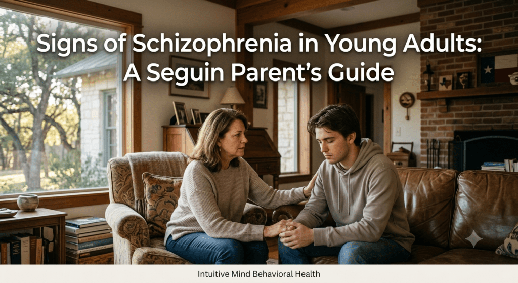 A compassionate photo of a mother with brown hair talking to her teenage son on a couch in a living room. Text at the top reads 'Signs of Schizophrenia in Young Adults: A Seguin Parent’s Guide'. Text in a small white banner below the image reads 'Intuitive Mind Behavioral Health'.
